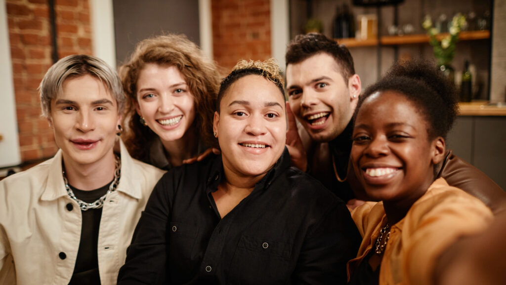 group of young cheerful friends posing for selfie in front of camera